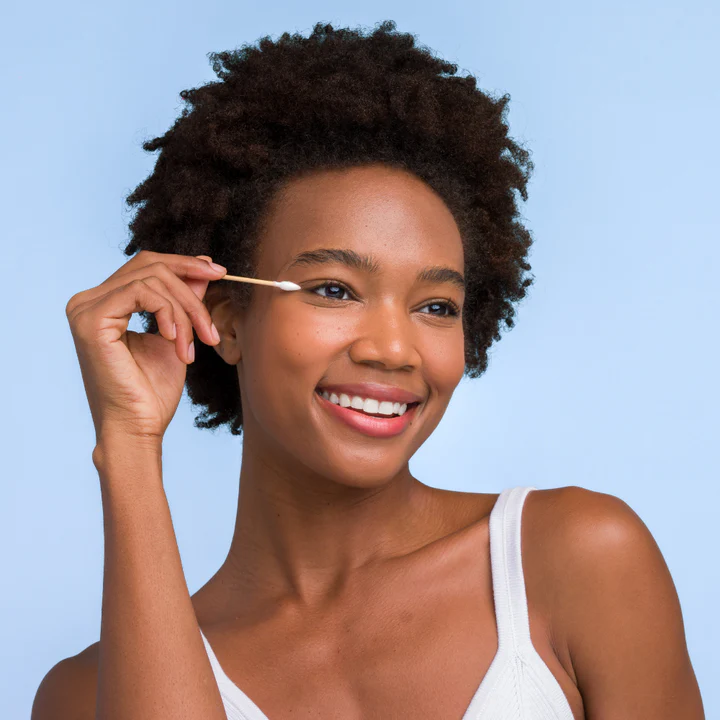 Woman using cotton swab for eye makeup touch-up.