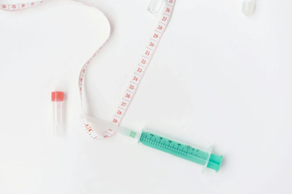 Syringe and measuring tape on white surface with small vial nearby