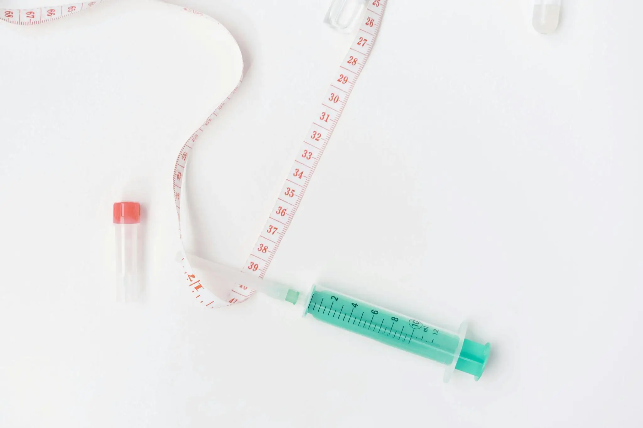 Syringe and measuring tape on white surface with small vial nearby